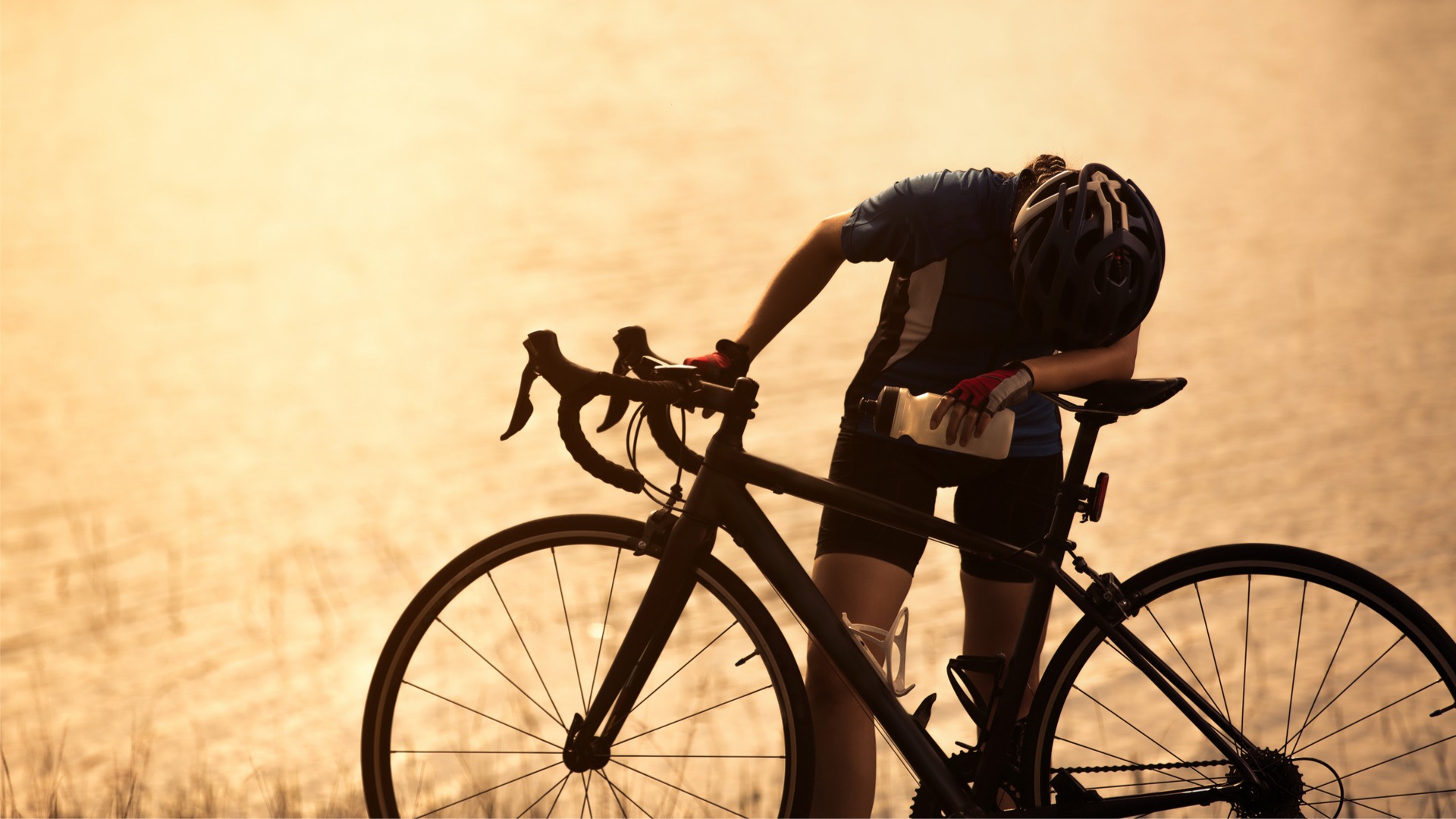 Cyclist in contemplation by the water during sunset.