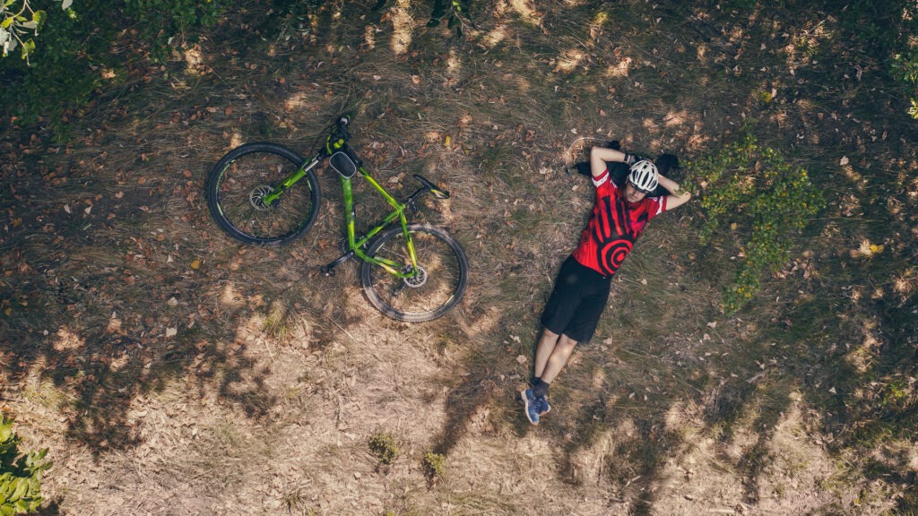 Cyclist laying next to their mountain bike in the forest, taking a restful break on the ground amidst a long ride.