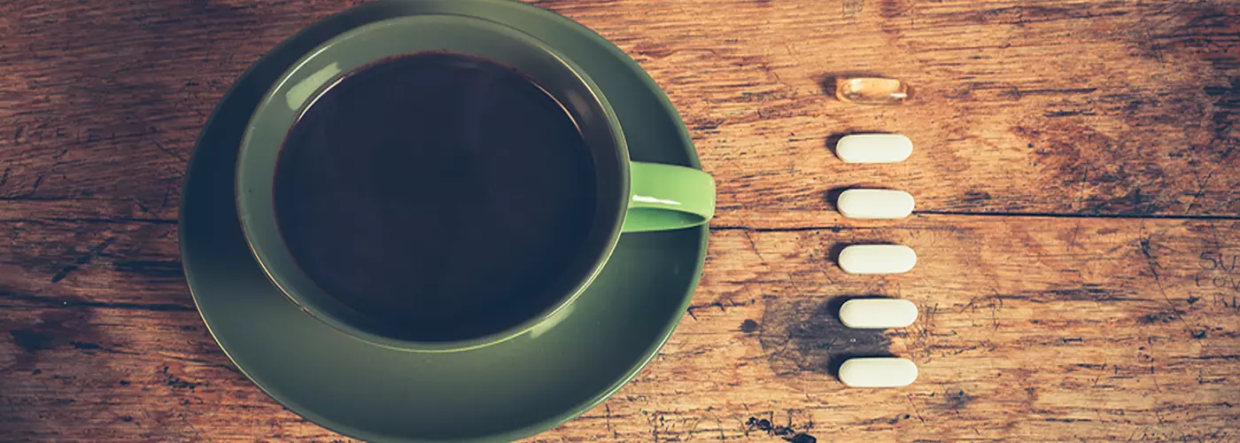 Cup of coffee beside energy supplements on a wooden table, representing a cyclist's morning ritual.