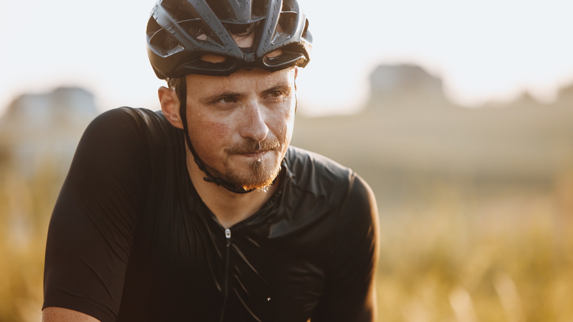 Close-up of a focused cyclist wearing a helmet, bathed in golden sunset light.