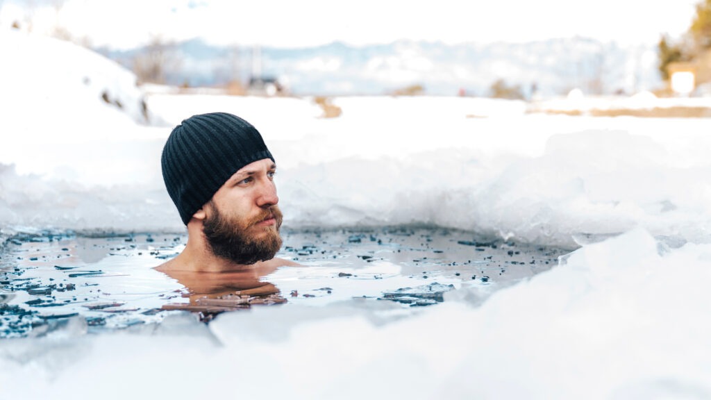 Man fully immersed in a freezing natural body of water, surrounded by snow.