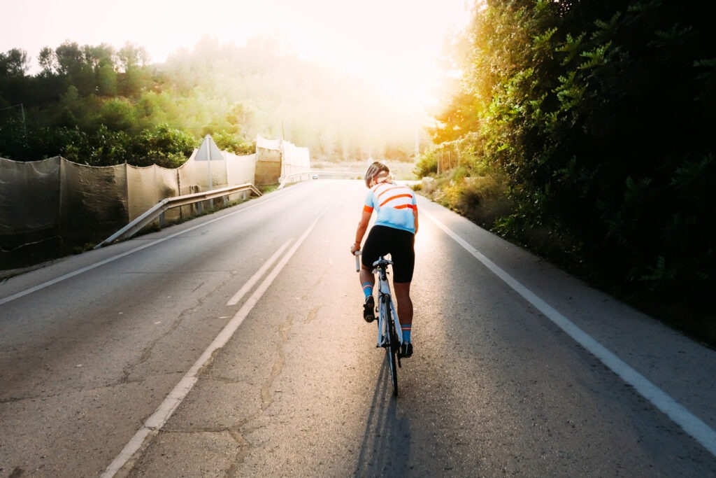 Cyclist in bright striped jersey powering through a road amidst nature during sunrise.